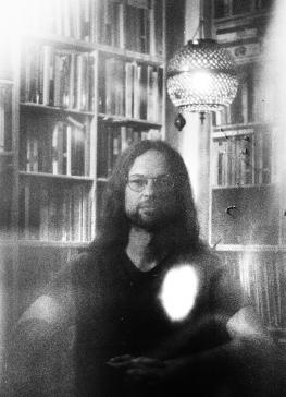 Black and white picture of Jacob Schmidt-Madsen, sitting in front of a bookshelf and beneath a mirror ball